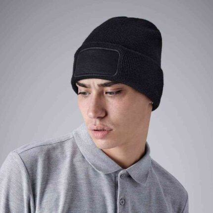 Junger Mann trägt eine schwarze Strickmütze mit aufgenähtem Patchfeld für individuellen Druck.