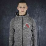 Junger Mann trägt eine graue Spiro S245M Microfleece-Hoodiejacke mit Meenzer derfe des-Stickerei auf der Brust vor dunklem Hintergrund.